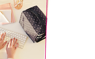 Die Beauty Bag, die man zum Start mit Mary Kay im November 2022 gratis erhalten kann, liegt auf einem Tisch neben einem Schreibblock, Wasserglas und einer Tastatur, auf der Hände mit rotem Nagellack tippen