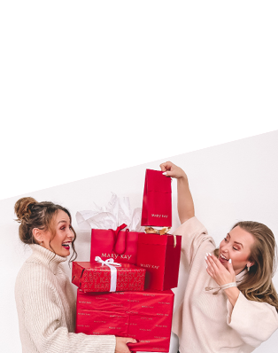 Zwei strahlende Frauen (selbständige Schönheits-Consultants mit Mary Kay) stapeln Geschenke, die in rotem Geschenkpapier eingepackt sind