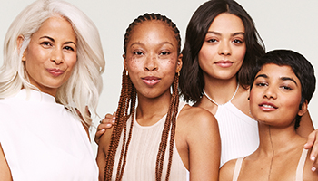 Vier Frauen unterschiedlichen Alters mit unterschiedlichem Teint, Haut- und Haarfarbe blicken frontal in die Kamera. Alle haben strahlende, reine Haut.