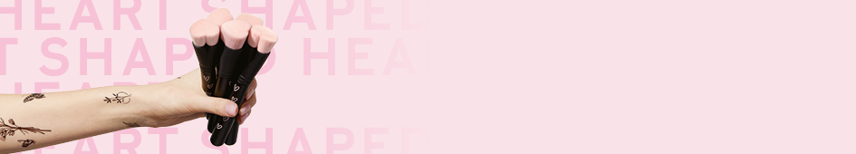 Eine Frauenhand hält fünf Mary Kay Heart-Shaped Foundation Brushes ins Bild – schwarze Pinsel zum Auftragen von Make-up mit rosa Pinselhaaren in Herzform, für die Mary Kay bei jedem Verkauf an FLY & HELP spendet.