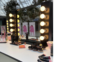 Eine Vielzahl der Mary Kay Make-up Produkte liegen auf einem Schminktisch vor einem beleuchteten Make-up-Spiegel.