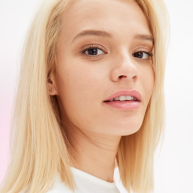 Ein weibliches Model mit mittlerem Hautton und blonden Haaren und natürlichem Make-up blickt in die Kamera