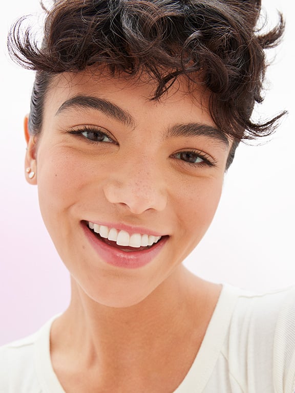 Eine Frau mit dunklem Haar und mittlerer Haut schaut in die Kamera und lächelt