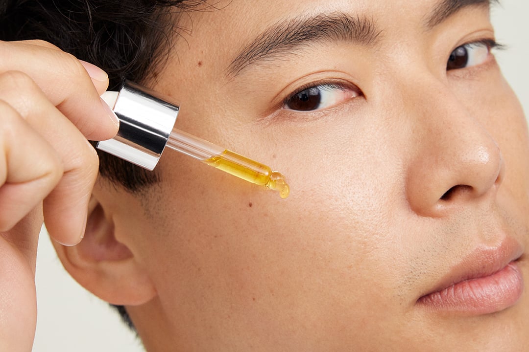 Nahaufnahme eines Mannes, der Mary Kay Nourishing Oil mit einer Pipette auf seine Wange aufträgt