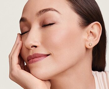 A smiling young woman has her eyes closed and rests her face in her hand