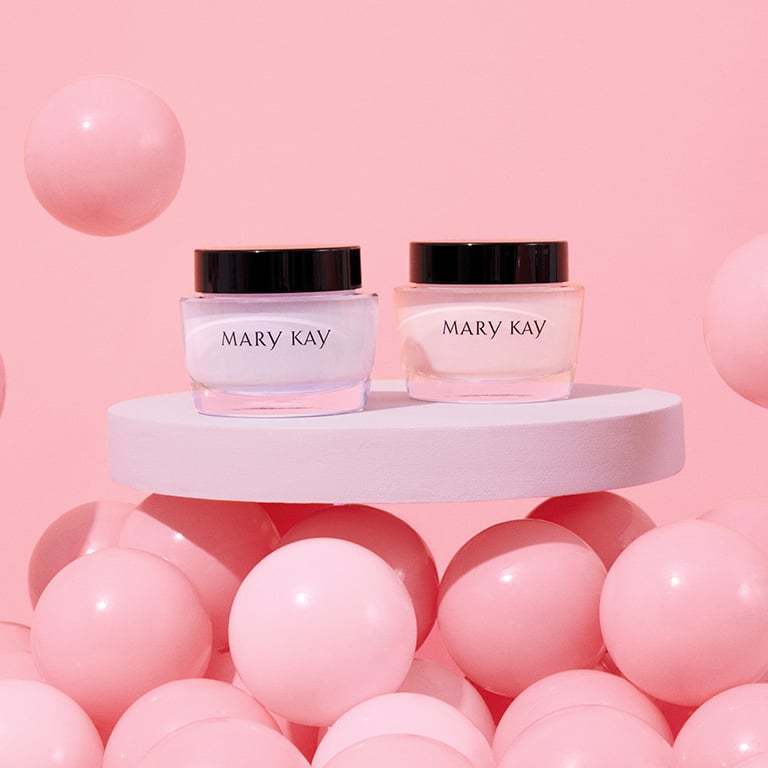 Tiegel mit Mary Kay Oil Free Hydrating Gel und Mary Kay Intense Moisturizing Cream stehen auf einem weißen Tisch, umgeben von rosa Luftballons