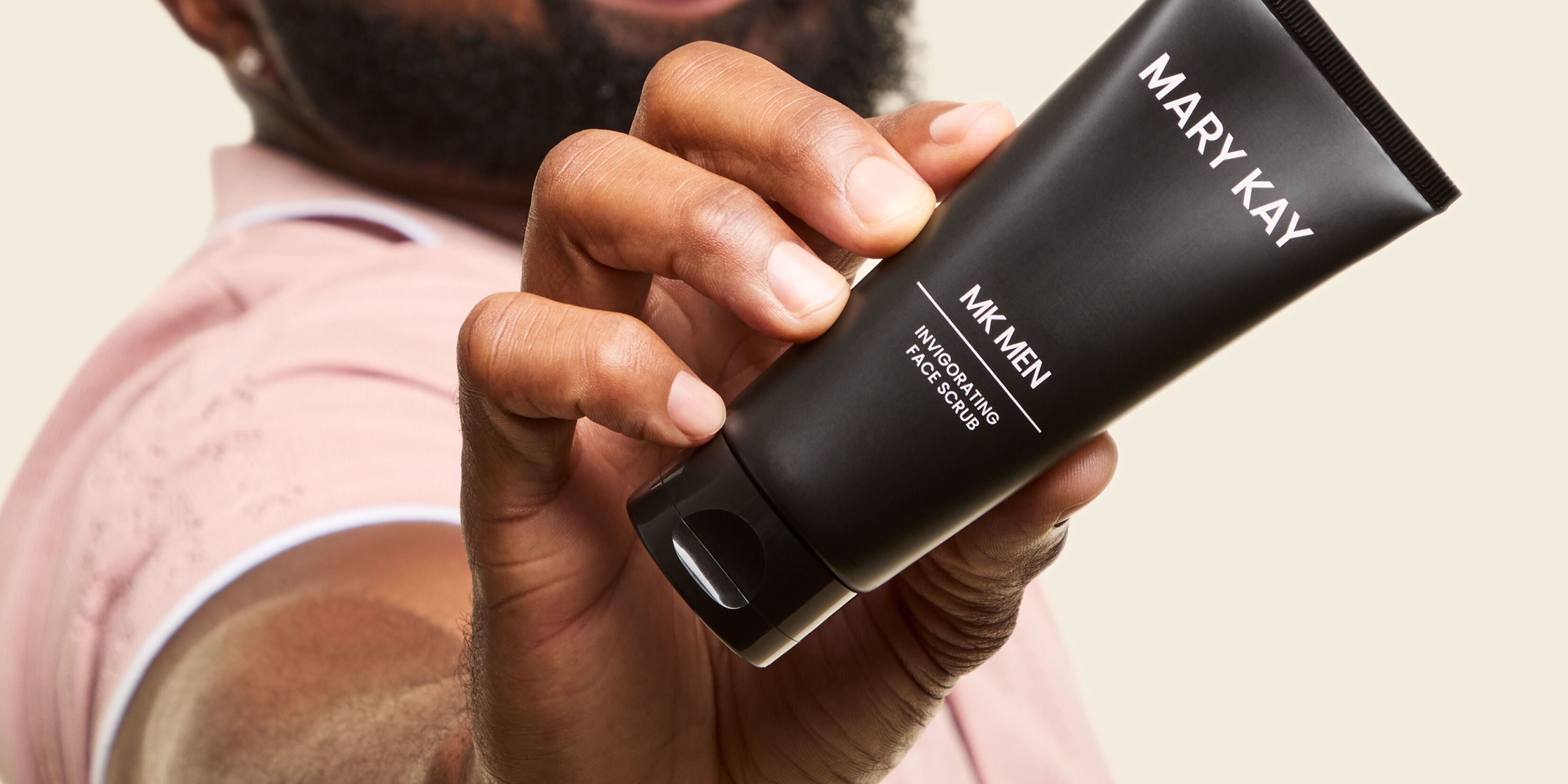 Ein Mann h&auml;lt die schwarze Tube des MK Men Invigorating Face Scrub von Mary Kay in die Kamera