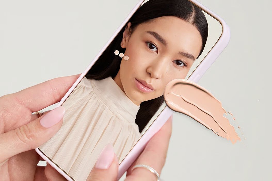 Eine Frau benutzt das Foundation Matching Tool auf ihrem Handy. Au&szlig;erdem sieht man einen Foundation Smudge.