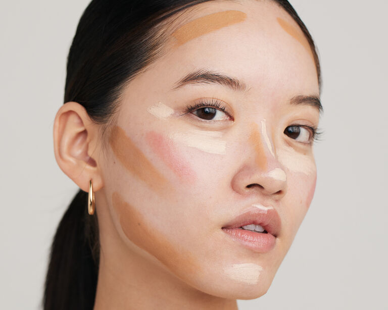 Eine Frau, die deutlich sichtbar im Gesicht Concealer, Contouring, Blush und Foundation aufgetragen hat (die Produkte sind noch nicht verblendet)