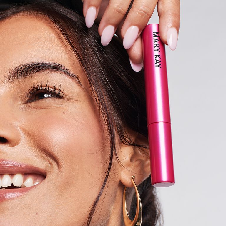 Eine Frau h&auml;lt die pinke Tube der Mary Kay Lash Love Fanorama Define + Lift Mascara neben ihr Gesicht