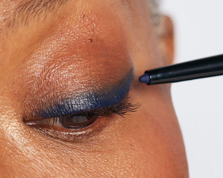 Nahaufnahme: Mit einem blauen Eyeliner wird ein Lidstrich auf dem halb geschlossenen Auge einer Frau aufgetragen