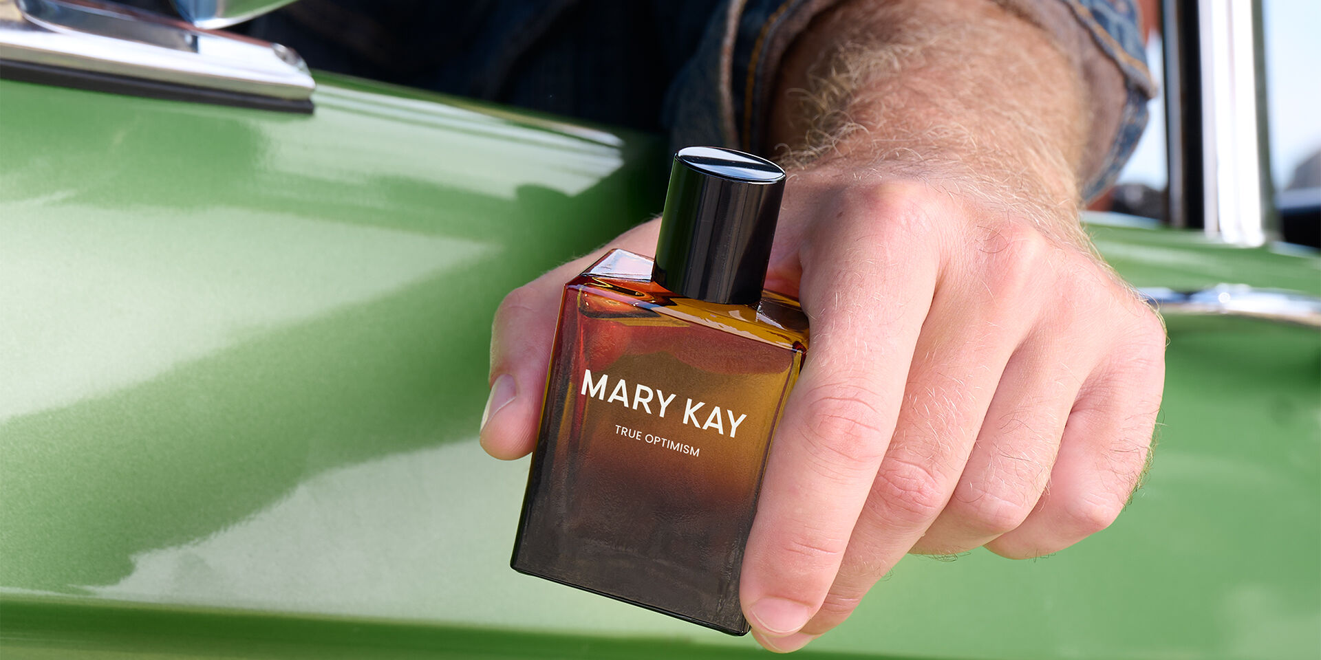 Eine Hand h&auml;lt Mary Kay True Optimism Eau de Parfum vor einem gr&uuml;nen Fahrzeug