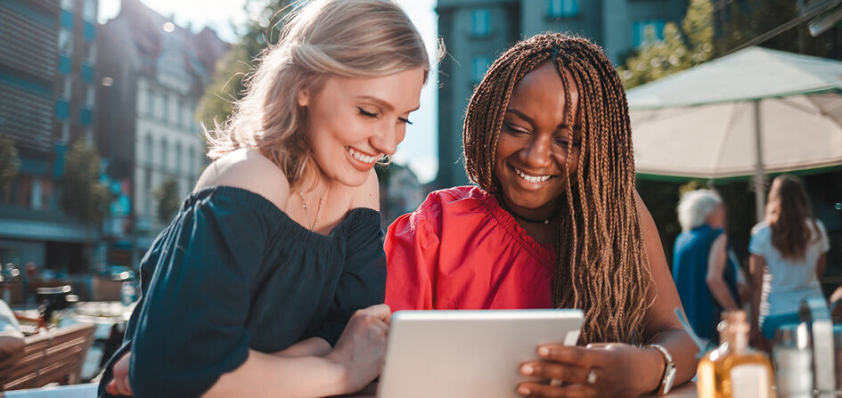 Zwei Frauen sitzen in einem Caf&eacute; in der Stadt und informieren sich mit einem Tablet &uuml;ber offene Stellen bei Mary Kay