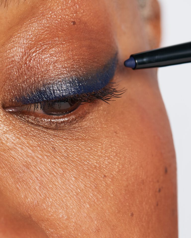 Nahaufnahme des Gesichts einer Frau: Mit einem blauen Eyeliner wird ein Lidstriche Wing