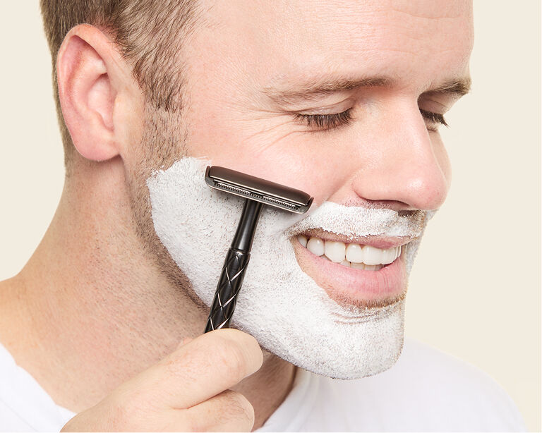 Nahaufnahme eines Mannes, der die Augen geschlossen hat und seinen Bart rasiert. Er hat dazu die wei&szlig;e MK Men Moisturizing Shave Cream von Mary Kay aufgetragen.