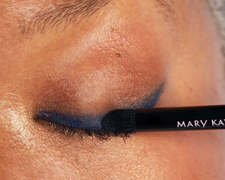 Nahaufnahme: Auf dem geschlossenen Auge einer Frau wird mit der Eye Smudger Brush von Mary Kay ein blauer Lidstrich (Eyeliner) verblendet