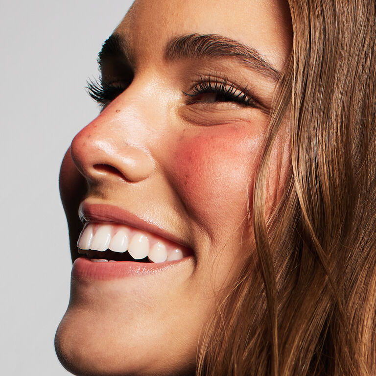 Seitliche Aufnahme einer Frau, deren Gesicht mit dem Strawberry Makeup Trend geschminkt ist: Fake Freckles, glowy skin und sonnengek&uuml;sste Wangen