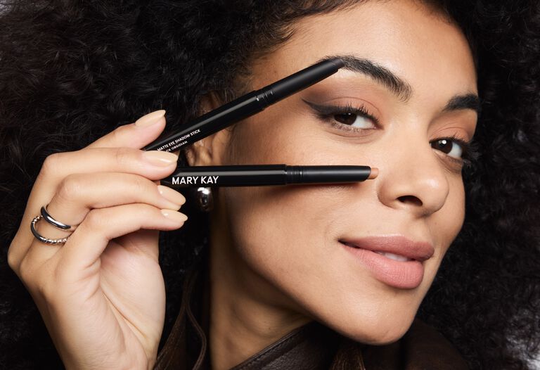 Eine Frau, die einen Make-up Look mit mattem Lidstrich tr&auml;gt, h&auml;lt in einer Hand zwei Matte Eye Shadow Sticks von Mary Kay in den Farben Celestial Nude und Black Obsidian