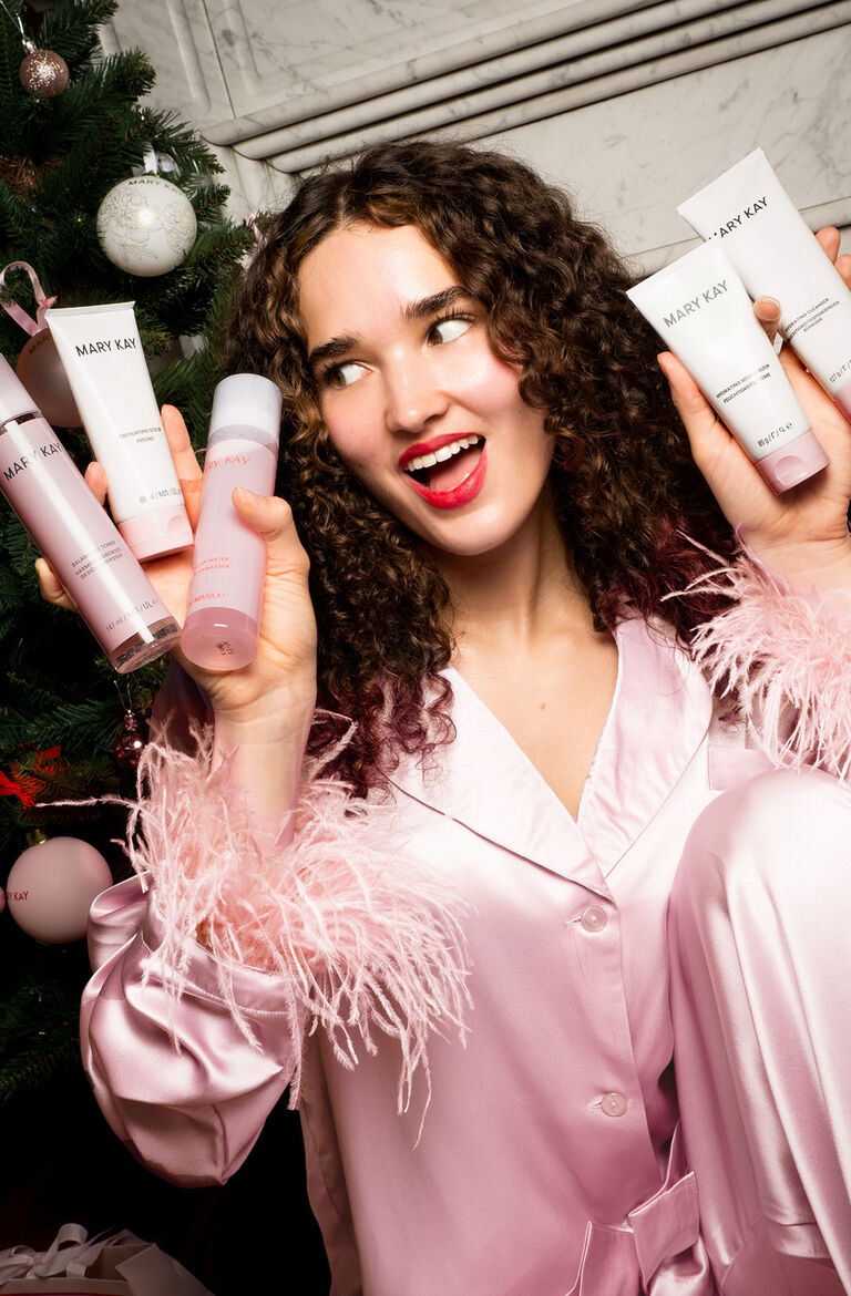 Eine Frau h&auml;lt Mary Kay Skincare Produkte in der Hand und freut sich. Hinter ihr ein Weihnachtsbaum.