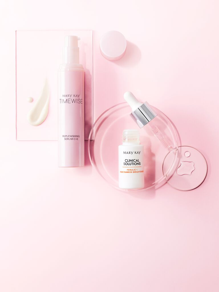 Zwei Mary Kay Hautpflege-Produkte in einem rosa Setting: TimeWise Replenishing Serum C + E und Clinical Solutions Booster Ferulic + Niacinamide Brightener