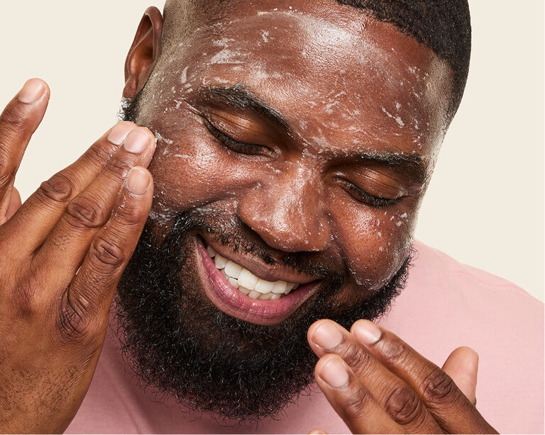 Nahaufnahme eines Mannes, der die Augen geschlossen hat und mit beiden H&auml;nden MK Men Invigorating Face Scrub im Gesicht verteilt (ein Gesichtspeeling)