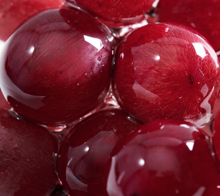 Saftig rote Trauben, die von einer durchsichtig gl&auml;nzenden H&uuml;lle oder Fl&uuml;ssigkeit umgeben sind