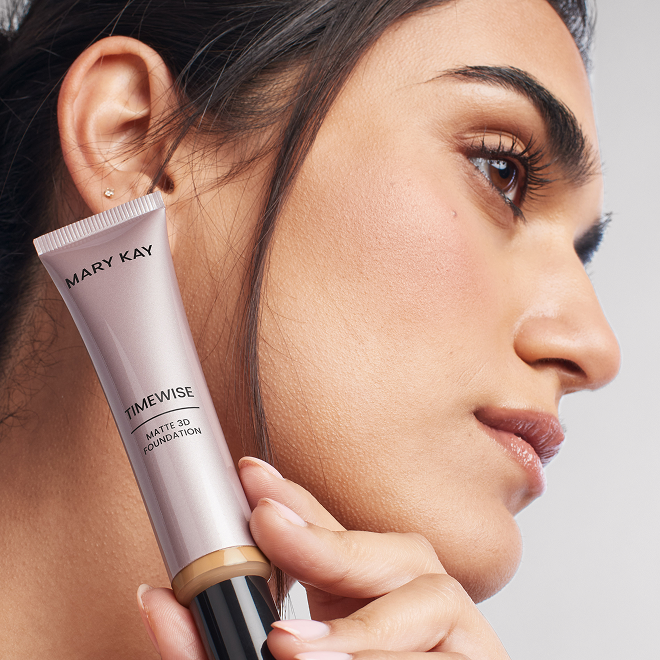 Eine Frau mit dunklem Haar pr&auml;sentiert die Mary Kay TimeWise&reg; Matte 3D Foundation neben ihrer Wange.