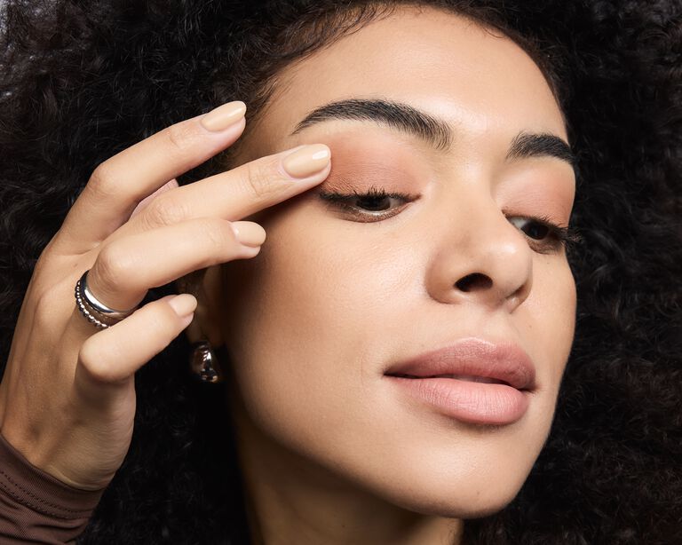 Nahaufnahme einer Frau, die mit dem Finger Eye Shadow auf ihr Augenlid tupft