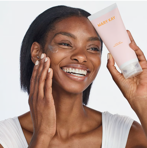 Eine l&auml;chelnde Frau in einem wei&szlig;en Oberteil cremt sich das Gesicht mit Sunscreen SPF 50+ von Mary Kay ein