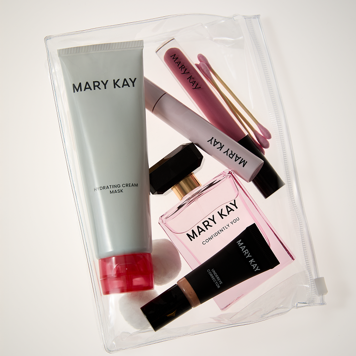 In einem durchsichtigen T&auml;schchen in Reisegr&ouml;&szlig;e sind einige Mary Kay Travel Essentials zu sehen: Hydrating Cream Mask, Confidently You Parfum, Unlimited Lipgloss, Great Heights Mascara, Undereye Corrector