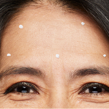 Eine Frau hat an f&uuml;nf Punkten auf der Stirn den TimeWise Repair Volu-Firm Deep Wrinkle Filler von Mary Kay aufgetragen